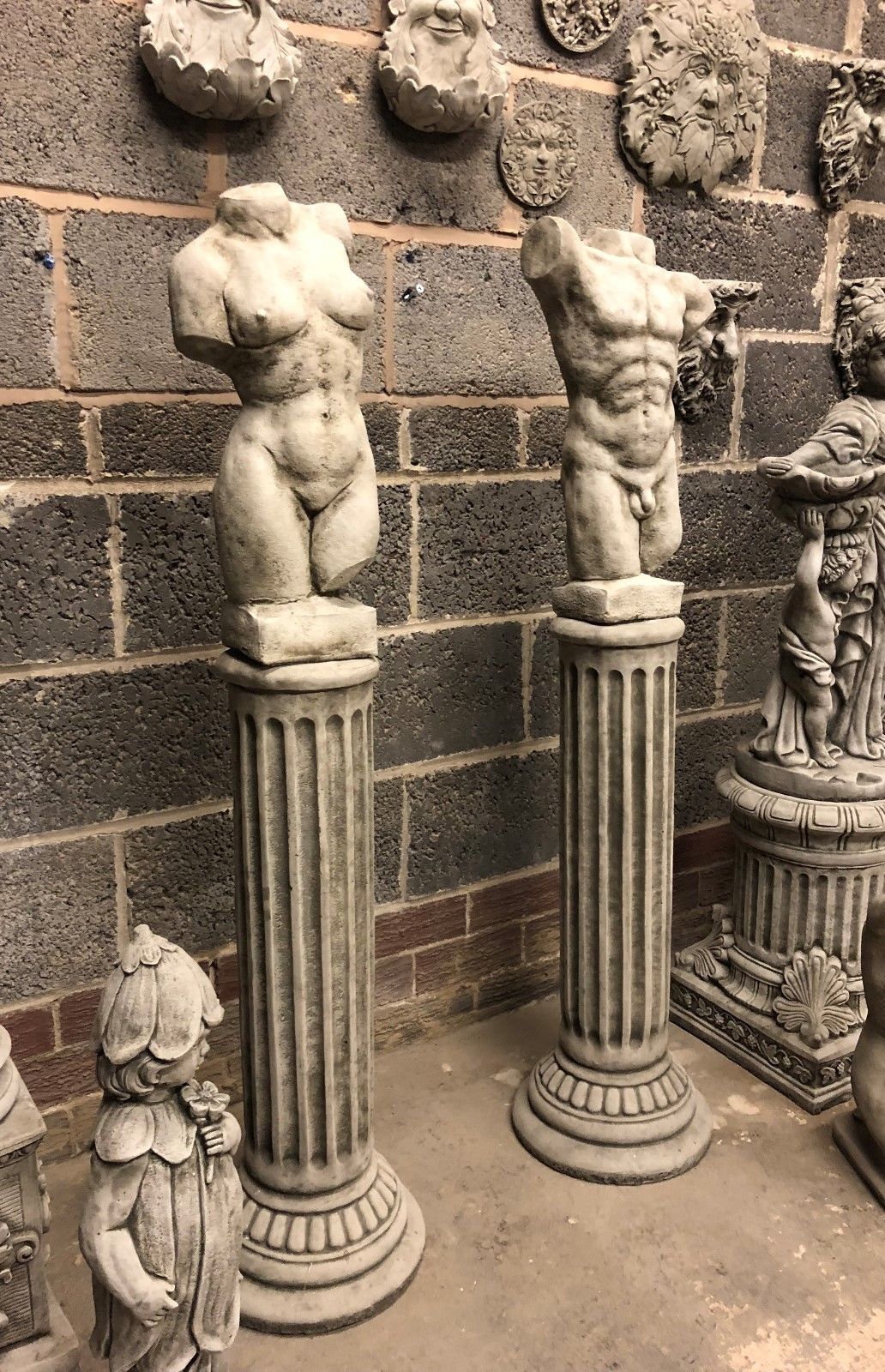 Stone garden torso statues on Grecian plinths, featuring male and female nude forms in antique grey finish. Ideal for outdoor weather-resistant decor.