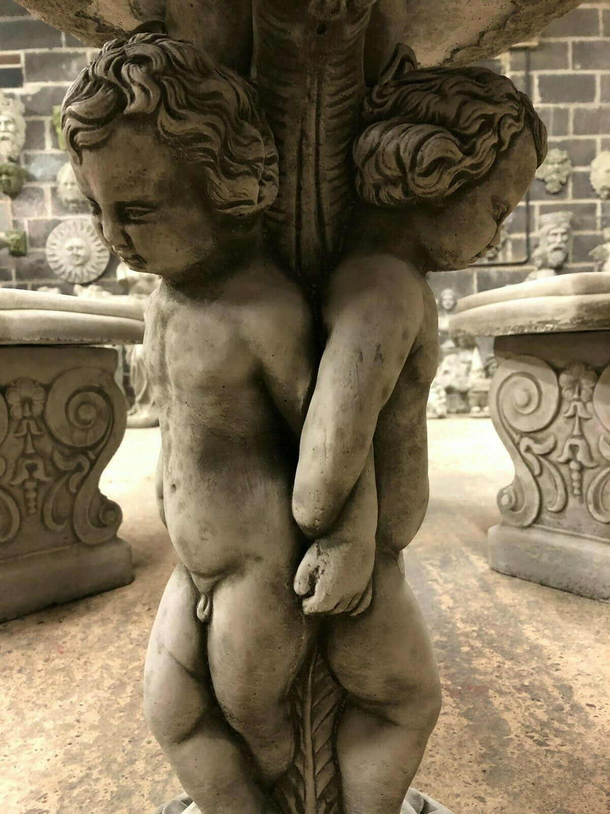 Close-up of detailed cherub figures supporting the Cherub Garden Bird Bath - Stone Antique Finish. Handcrafted limestone with antique texture.