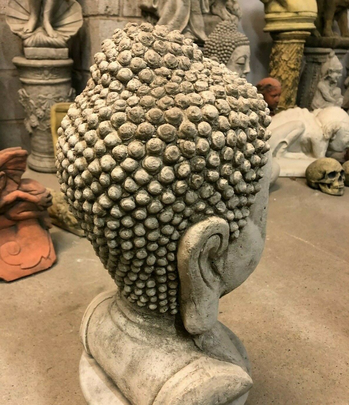 Rear view of Buddha head statue with textured stone curls and ear detail. Solid garden sculpture for peaceful outdoor ambiance.