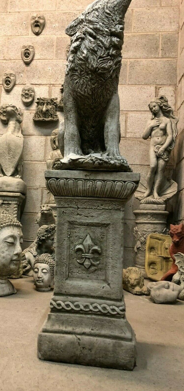 Low-angle view of Howling Wolf Statue on ornate stone pedestal, showcasing detailed craftsmanship and durable garden sculpture design.
