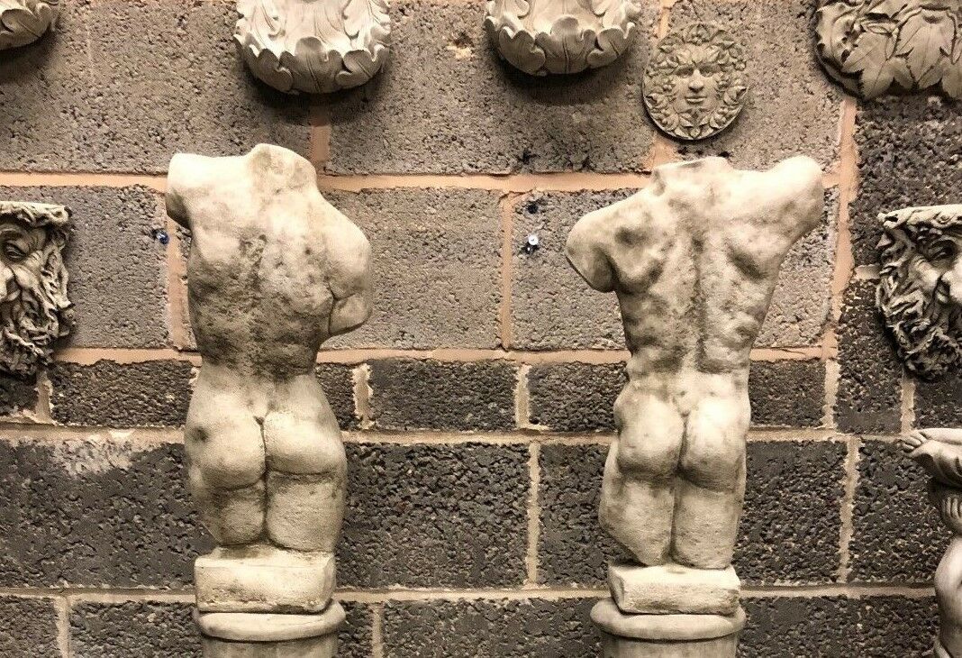 Rear view of paired torso statues on Grecian columns, showing anatomical detail. Stone garden sculptures with timeless design.