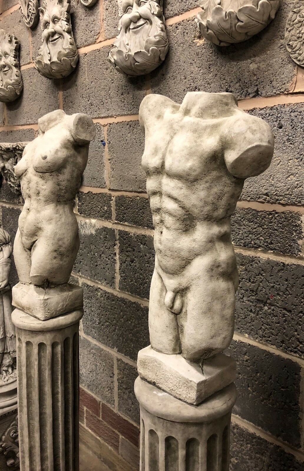 Angled view of torso statues on Grecian plinths, highlighting stone texture and classical form. Elegant garden ornaments for outdoor spaces.