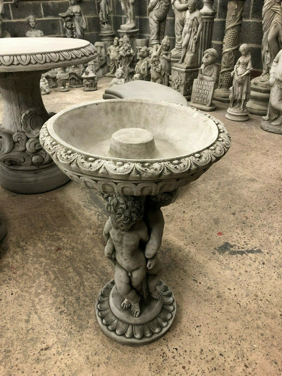 Angled view of Cherub Garden Bird Bath - Stone Antique Finish showing deep bowl and cherub trio support. Classic limestone garden feature.