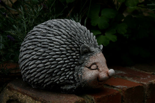Stone Hedgehog Garden Ornament with antique grey finish placed on a brick ledge. Durable outdoor decor for lawns and flowerbeds.