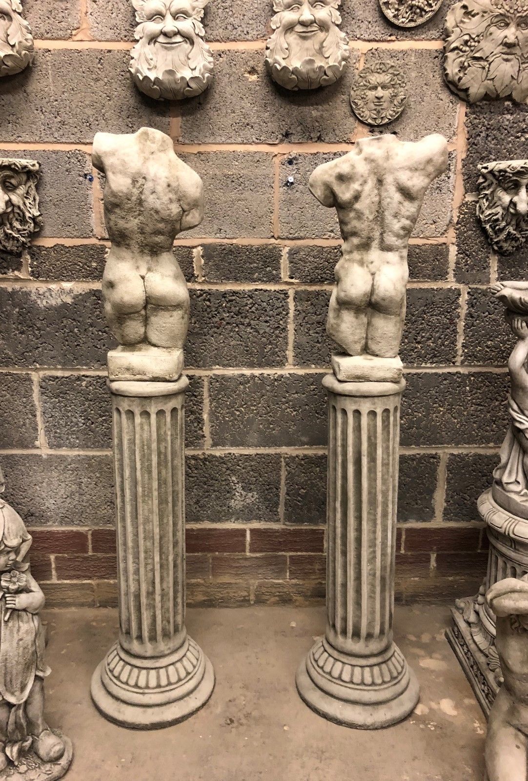 Rear view of torso statues on limestone plinths, emphasizing sculptural realism. Weather-resistant garden decor with antique finish.