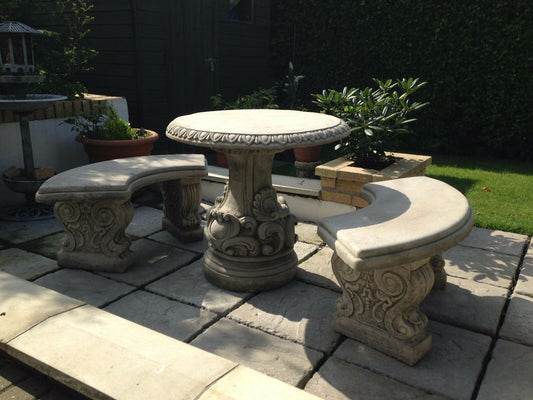 Solid stone garden table and bench set with scroll design on a patio. Features curved benches and ornate detailing, ideal for outdoor decor.