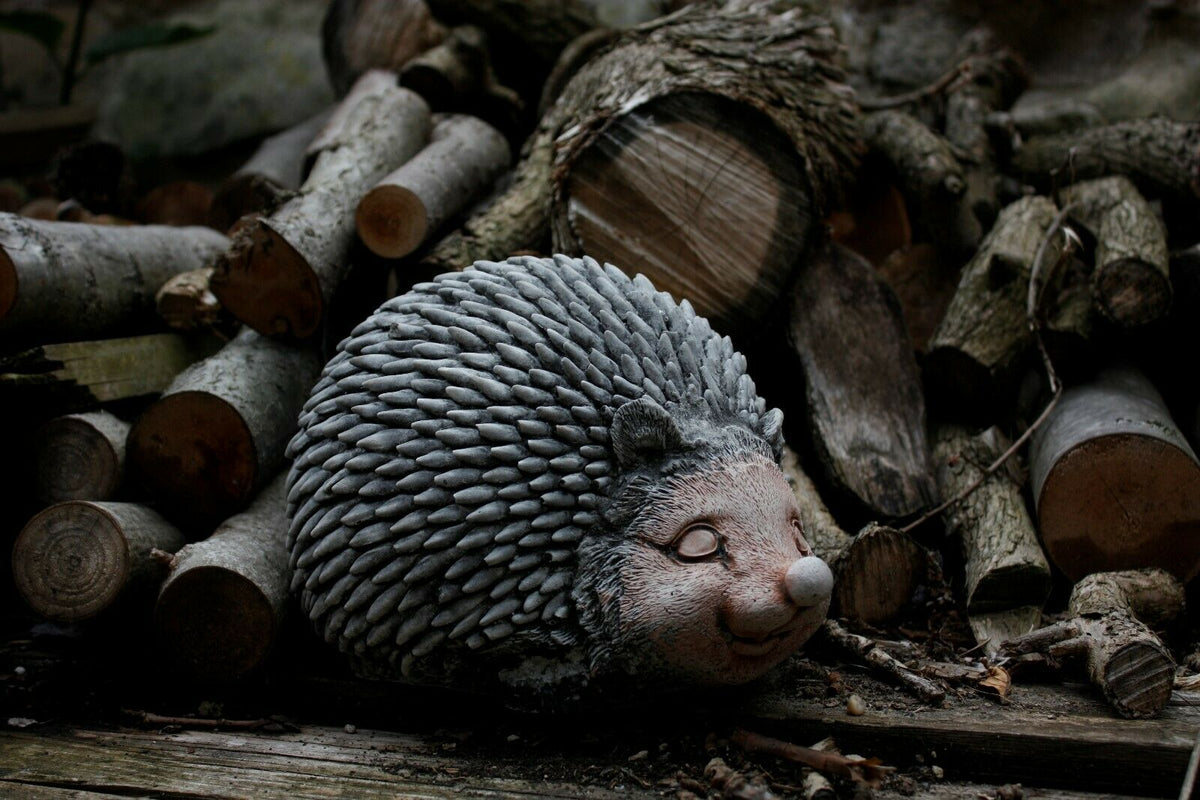 Smiling Stone Hedgehog Garden Ornament nestled among firewood. Handcrafted durable decor ideal for outdoor garden settings.
