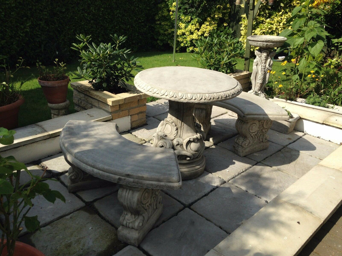 Stone garden table bench set with scroll design placed in a landscaped garden. Durable and decorative for patios and lawns.