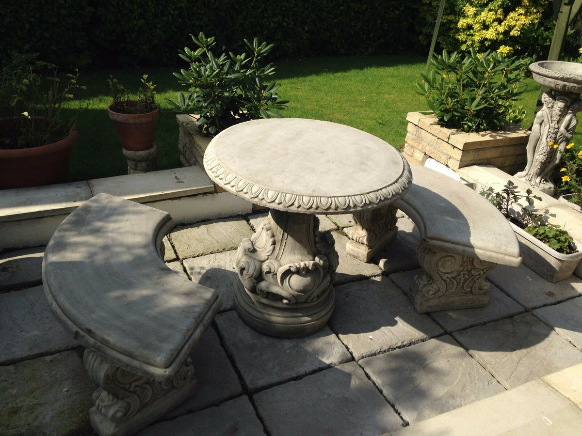 Curved stone benches and round table with intricate scrollwork. Heavy-duty garden furniture set for stylish outdoor seating.