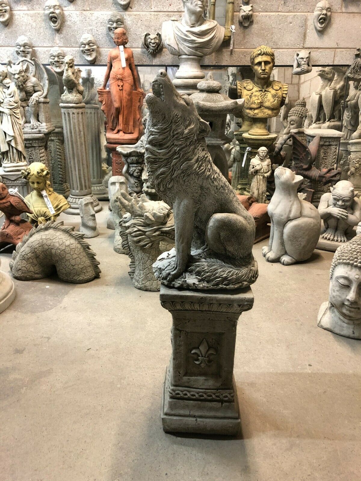Full view of Howling Wolf Statue on stone pedestal in a sculpture showroom, perfect for rustic garden or lawn ornamentation.