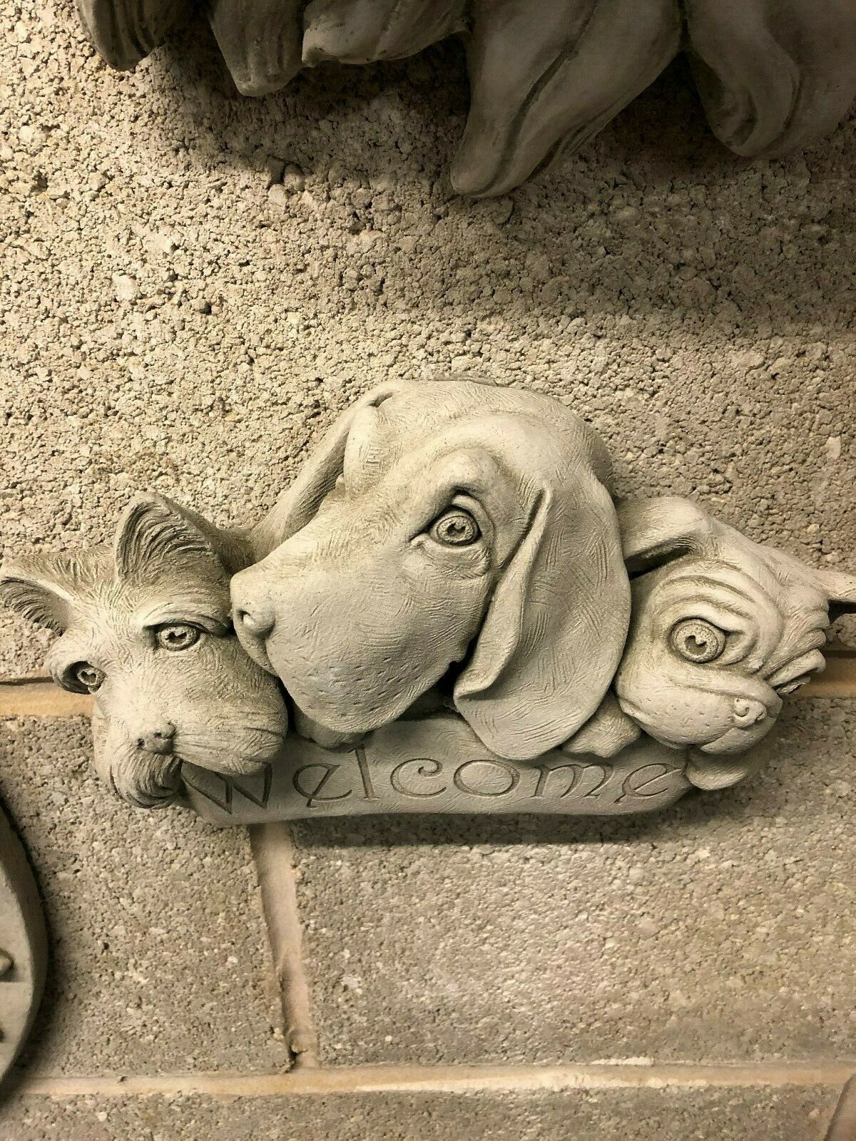 Front view of limestone Welcome Dog Garden Plaque with three sculpted dog heads, designed for outdoor decorative use in home gardens.