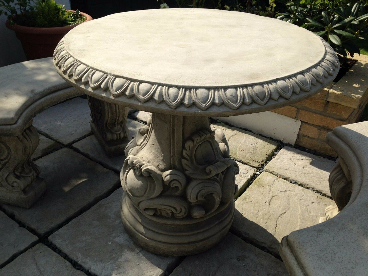 Close-up of solid stone garden table with carved scroll design. Elegant centerpiece for garden or patio seating areas.