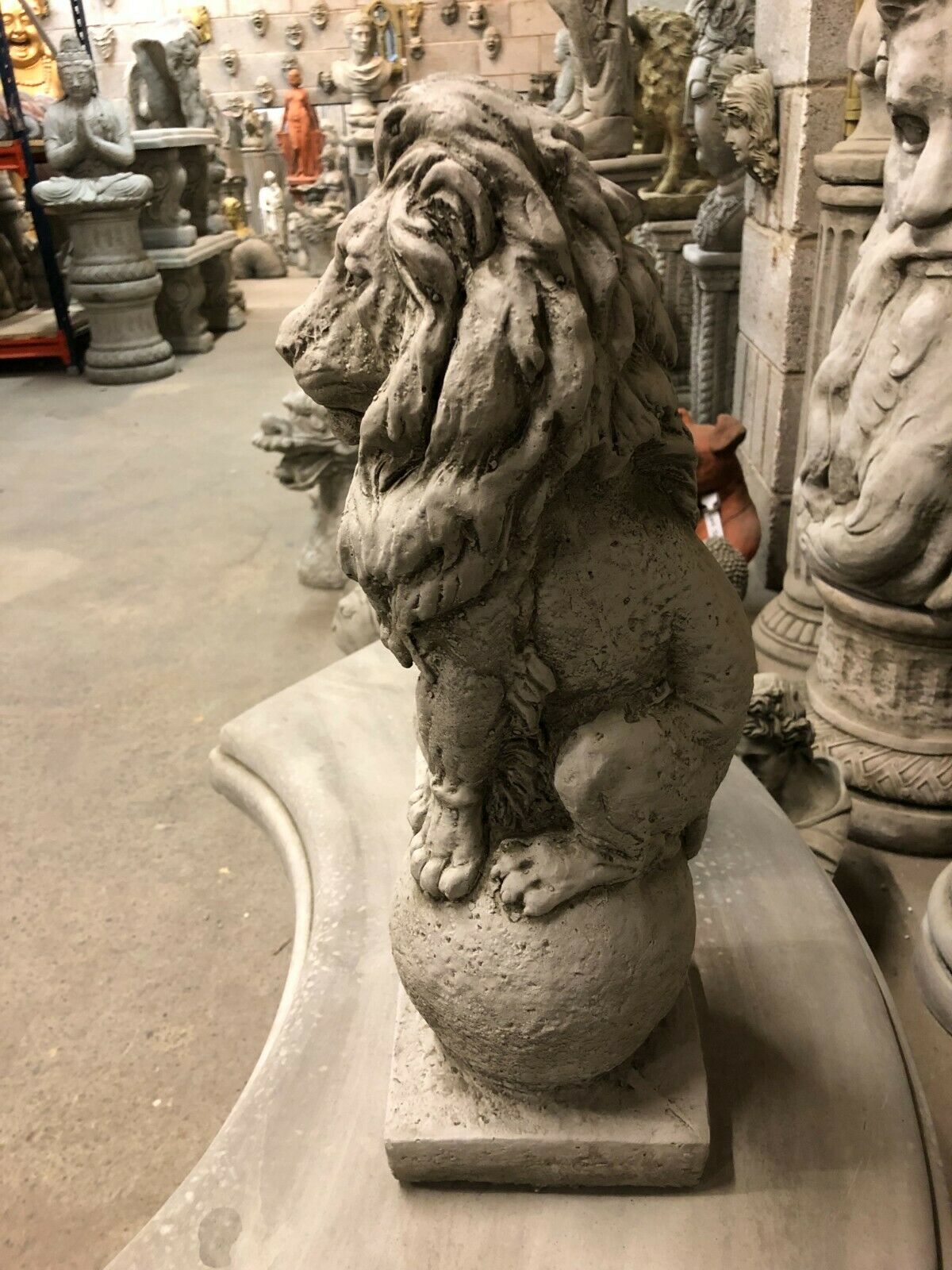Side view of a stone lion statue sitting on a ball, showcasing detailed mane and weather-resistant limestone texture for timeless garden decoration.