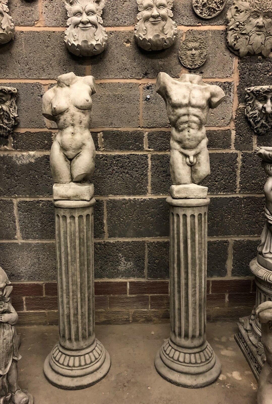 Pair of limestone torso sculptures with detailed male and female anatomy on fluted Grecian columns. Elegant stone garden ornaments for patios or lawns.