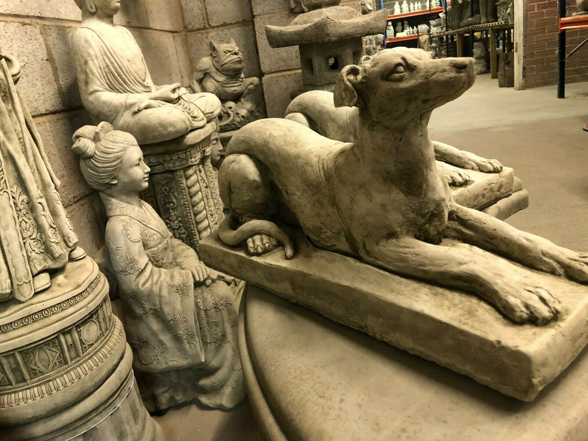 Stone Laying Greyhound Dog Statue surrounded by other garden sculptures, perfect for enhancing classic garden aesthetics.