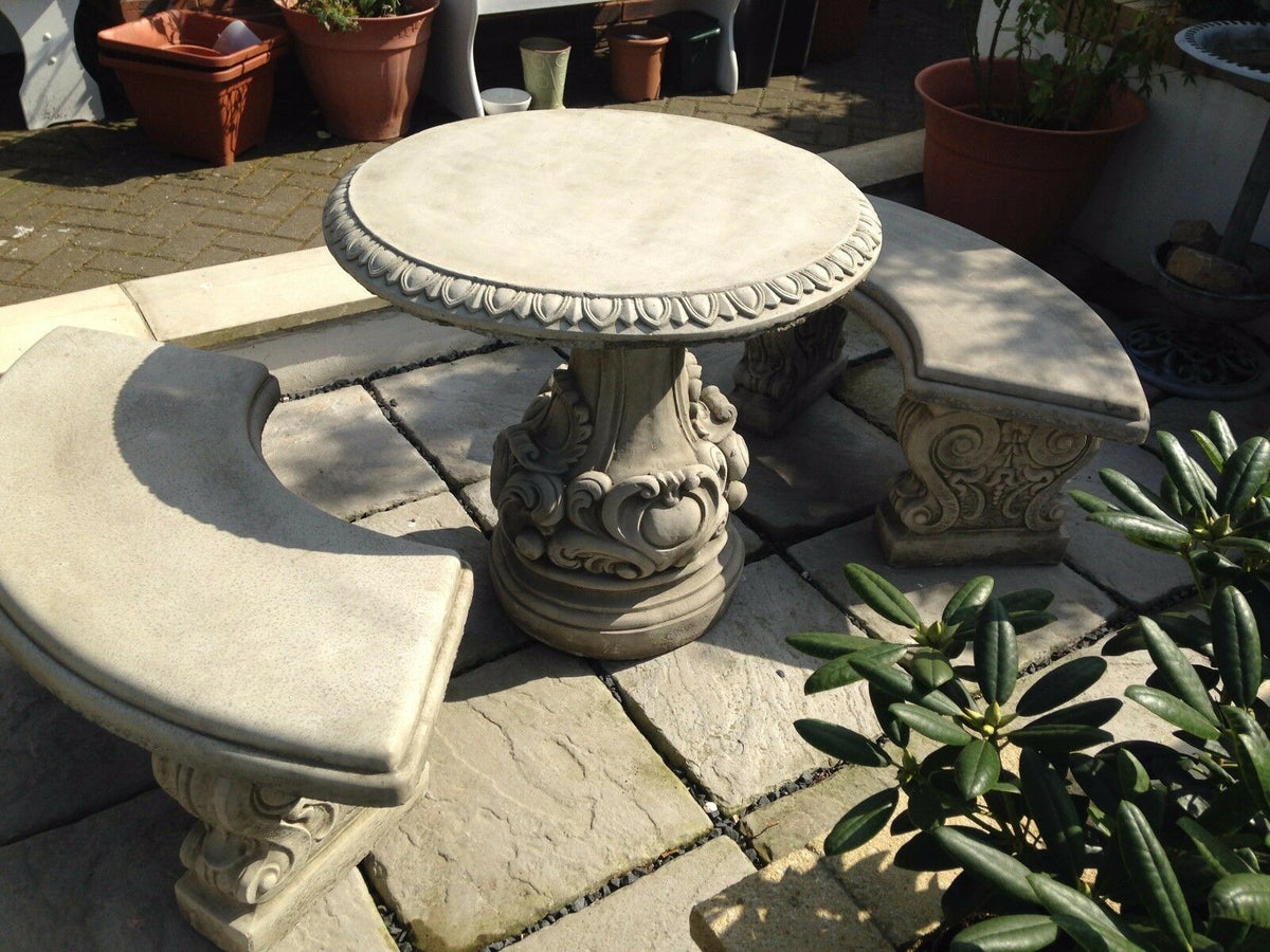 Handcrafted stone garden seating set with round table and two curved benches. Features detailed scrollwork for classic outdoor charm.