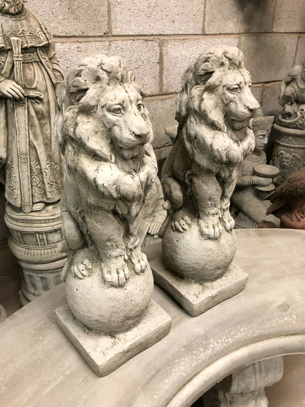 Two stone lion statues with regal posture on round bases, perfect as garden finials or patio entrance decor in home and garden settings.