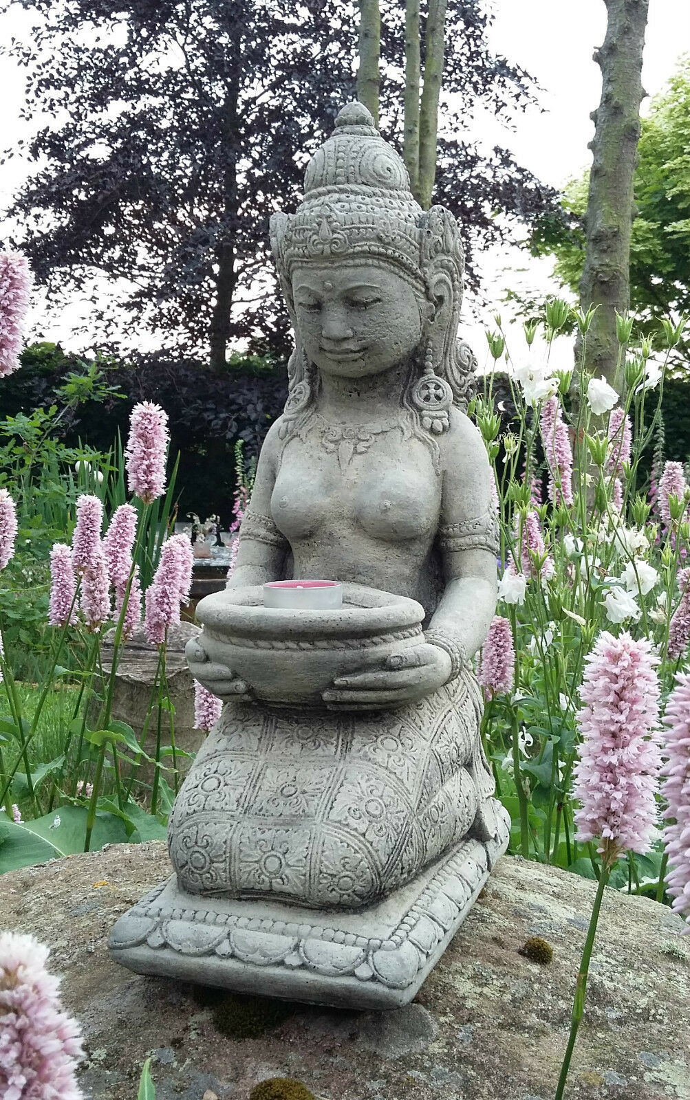 Front view of Stone Praying Geisha Statue with tealight holder, surrounded by blooming garden flowers, perfect for zen garden ambiance.