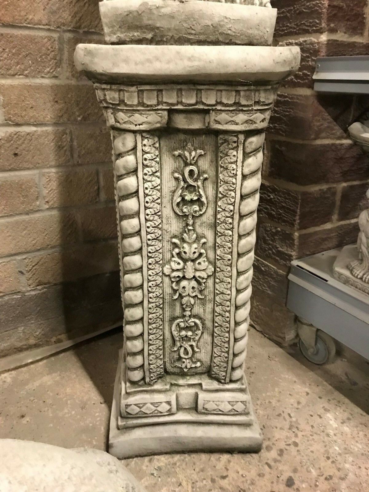 Close-up of the ornate stone plinth base supporting the Phoenix statue. Features floral and rope detailing for elegant garden presentation.