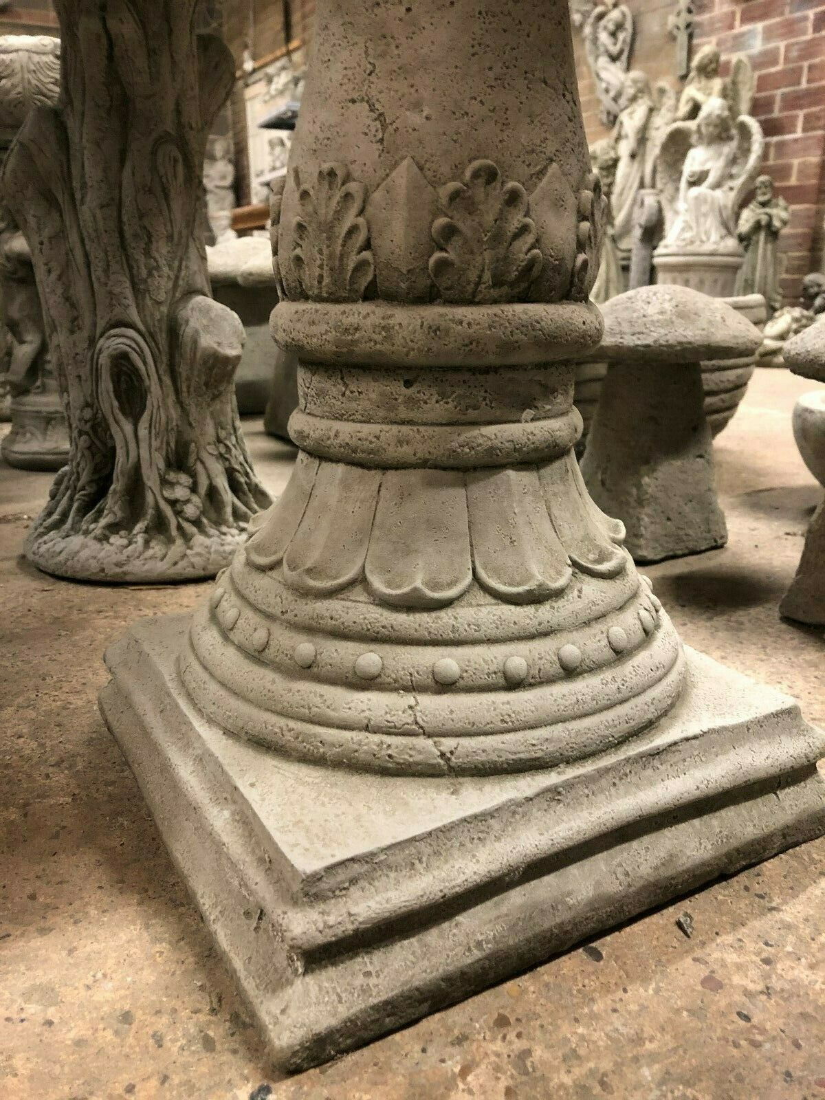 Close-up of antique finish base on Stone Traditional Style Garden Bird Bath. Features ornate leaf and bead detailing on a square pedestal.