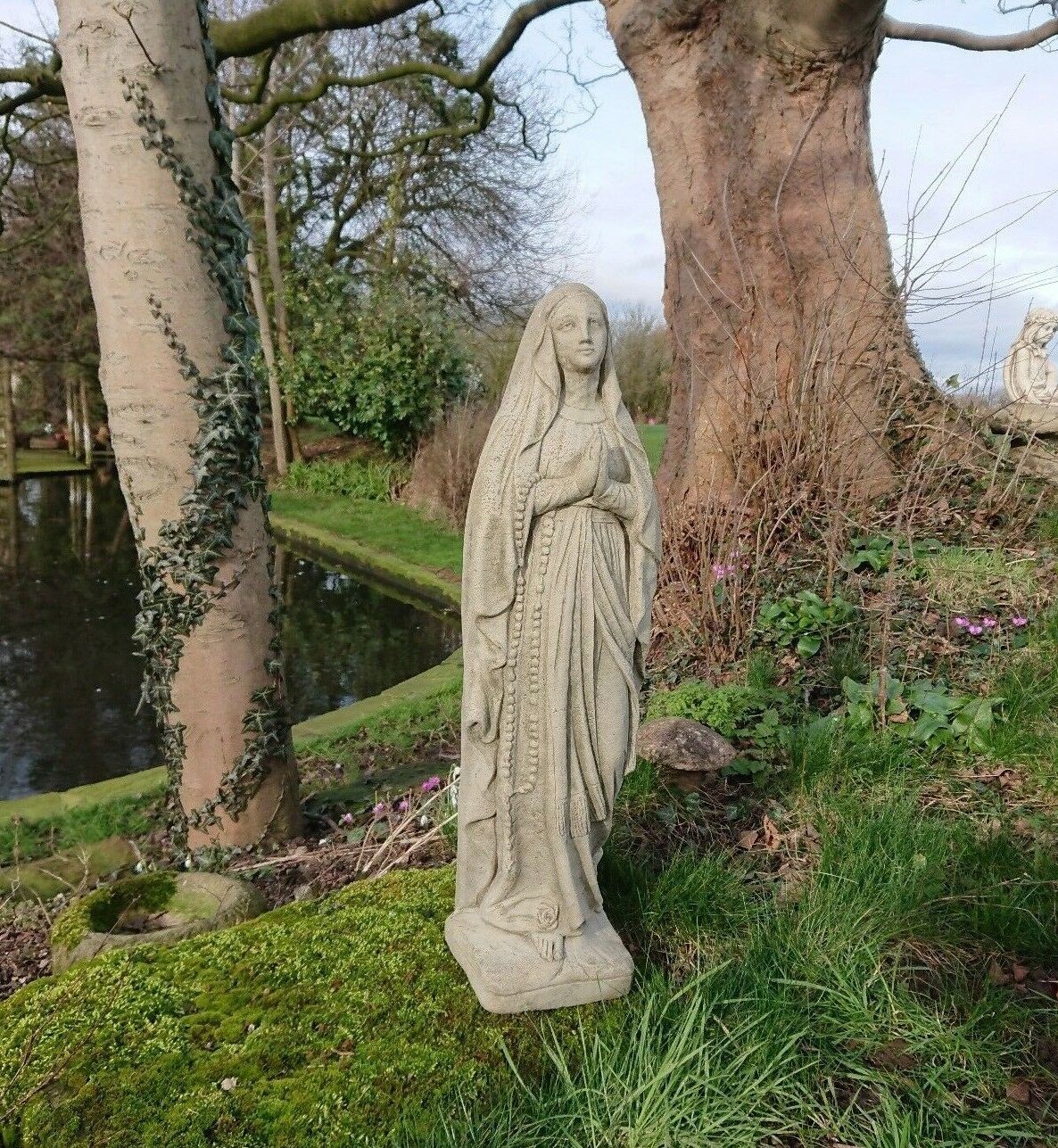 Antique-style Virgin Mary statue made of solid stone, displayed on a grassy lawn. Elegant religious sculpture for home or garden.