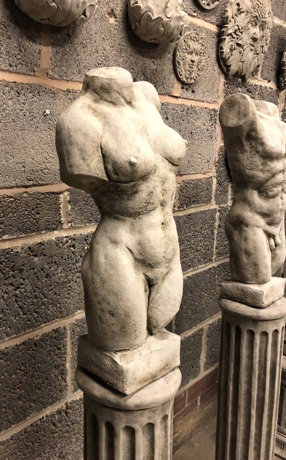 Angled view of female torso statue on limestone plinth, highlighting textured stone surface. Weather-resistant garden ornament with classical appeal.