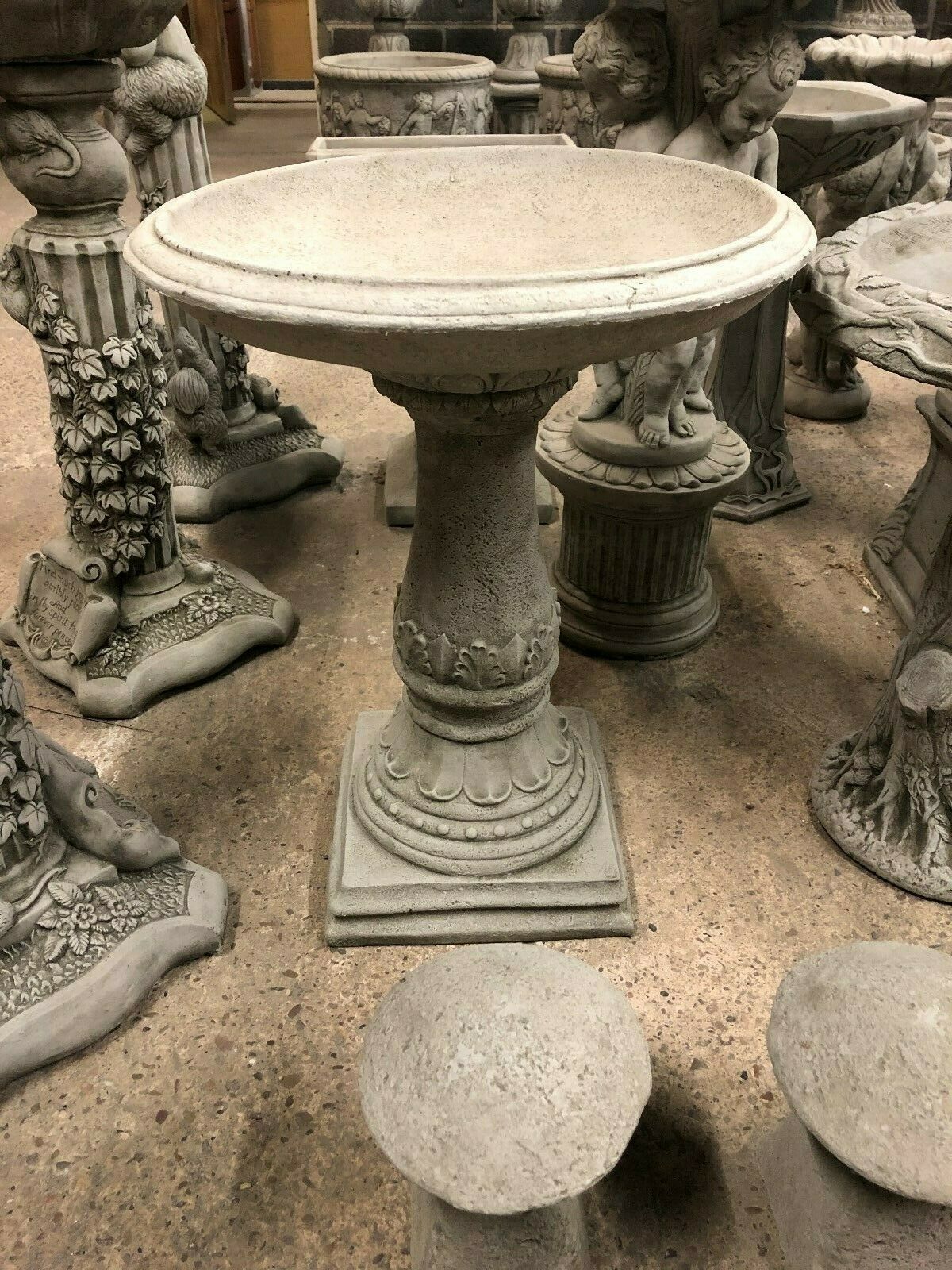 Full view of Stone Traditional Style Garden Bird Bath with antique finish, surrounded by other stone garden ornaments. Heavy and weather-resistant.