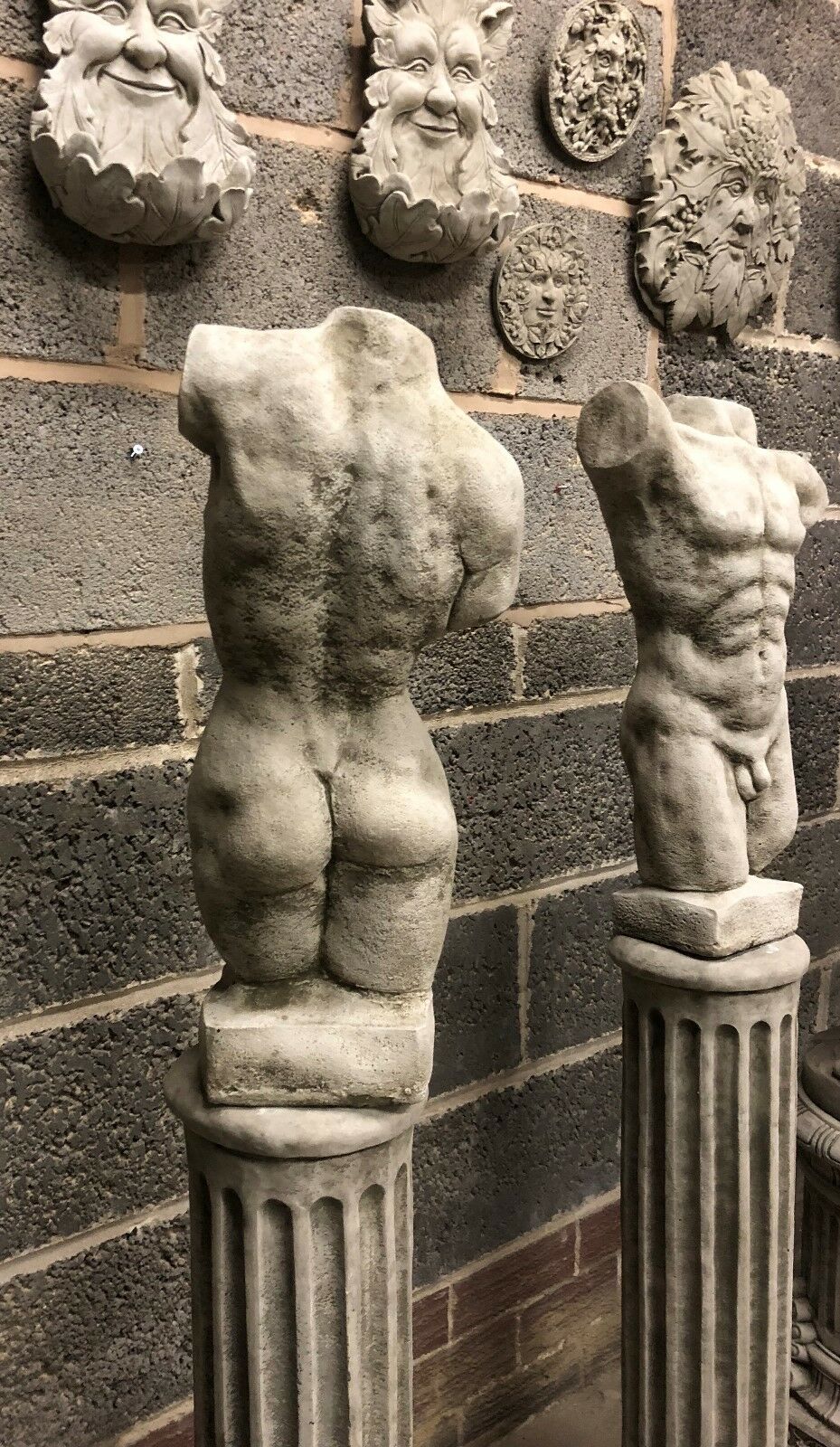 Back view of male torso statue on Grecian column, showing muscular detail and antique stone texture. Ideal for outdoor classical garden themes.