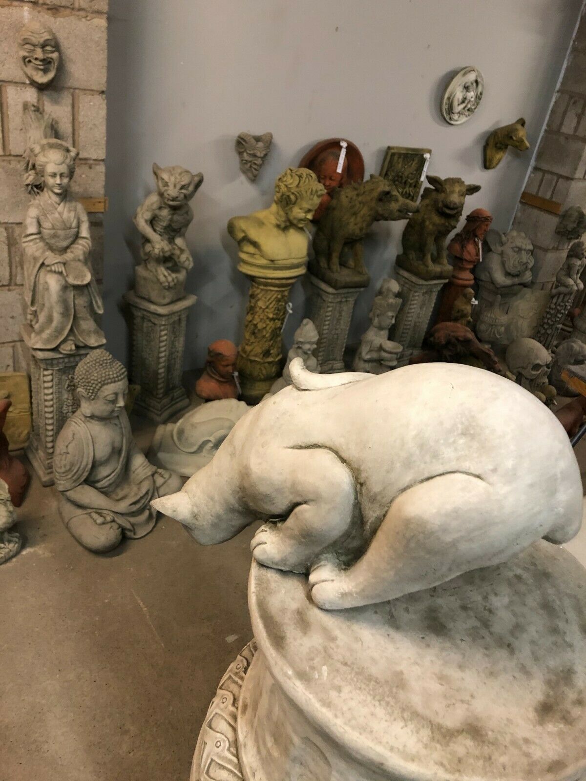Side angle of Pouncing Cat Garden Statue on stone base, surrounded by various decorative garden sculptures.