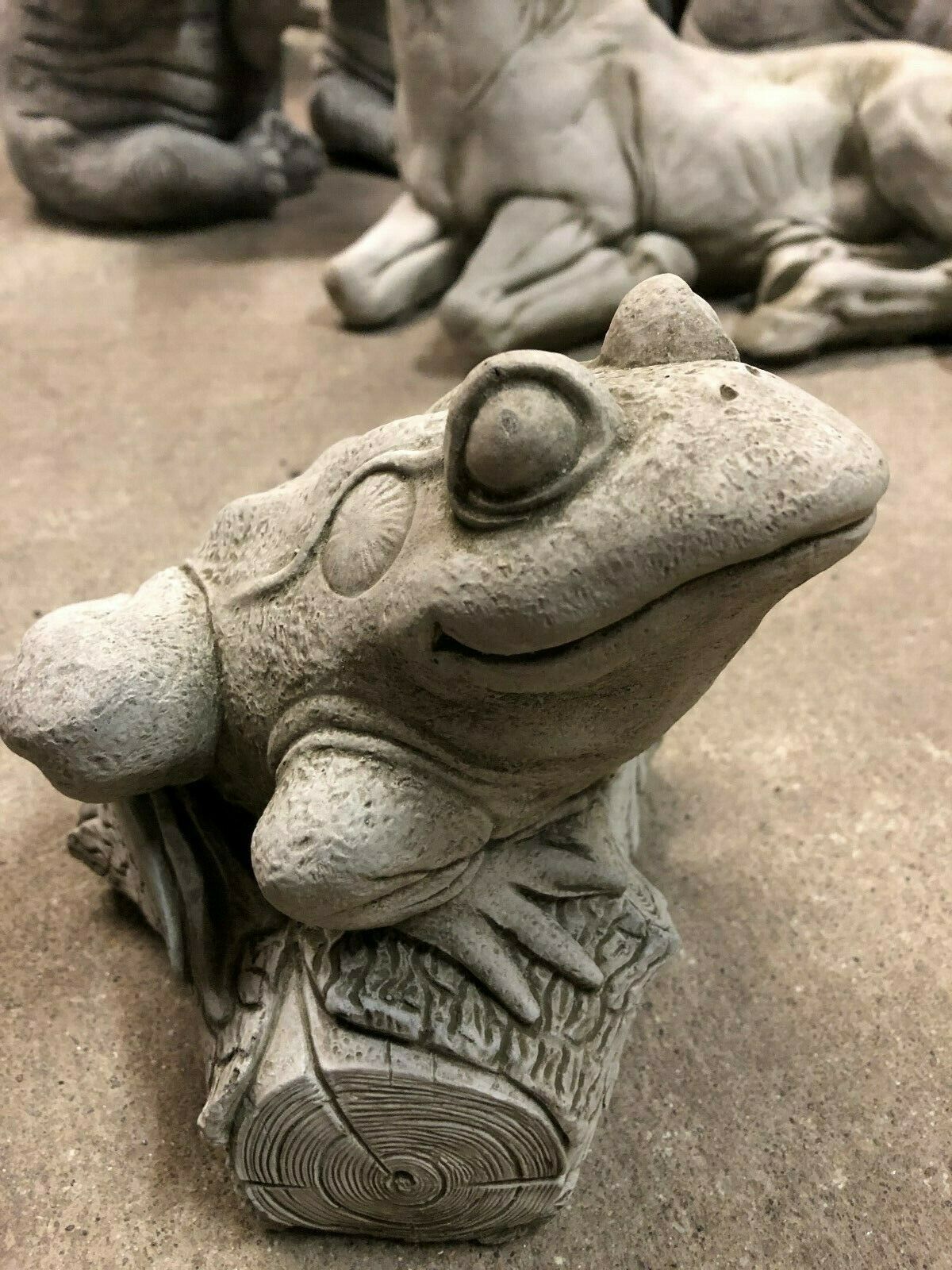 Close-up of smiling stone frog garden ornament on log, crafted from durable limestone for year-round outdoor display.