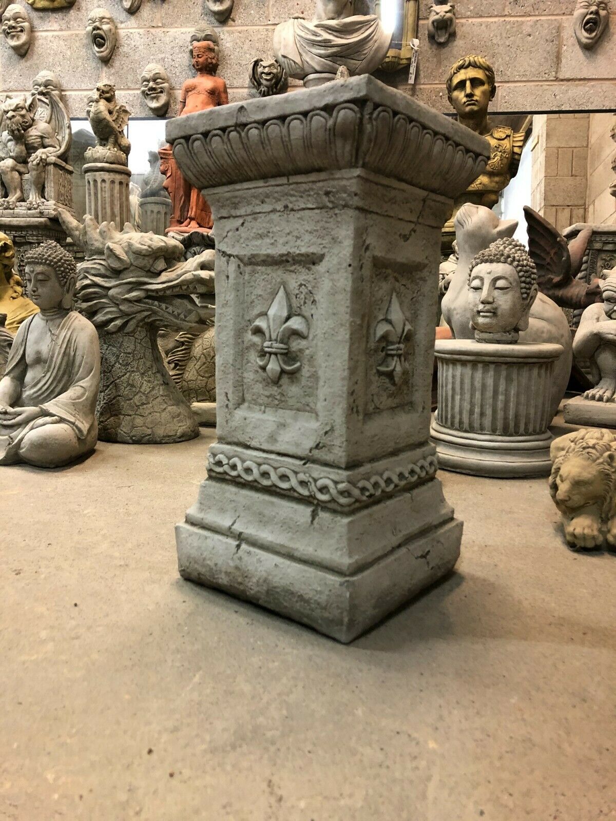 Weather-resistant Stone Fleur De Lis Garden Pedestal with decorative carvings, perfect for showcasing statues in home or lawn decor settings.