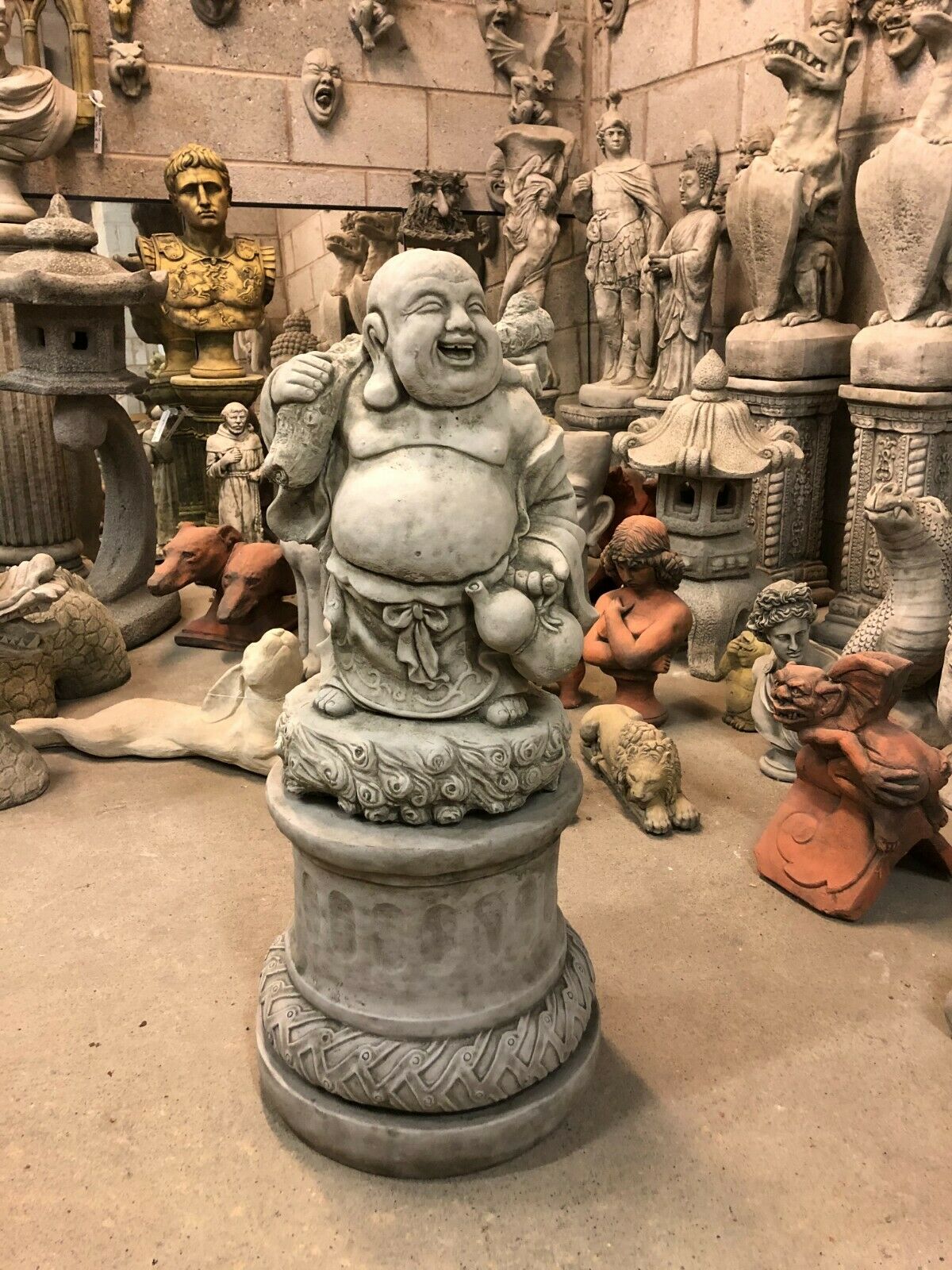 Laughing Buddha Statue - Stone Plinth | Limestone Finish, featuring a joyful Buddha figure with sack on shoulder, ideal for garden decor and good fortune.