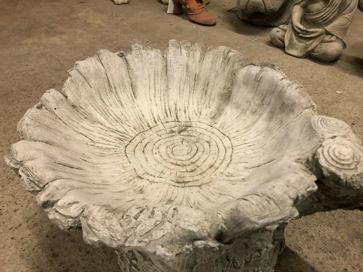 Close-up of stone tree stump bird bath showing intricate wood grain and ring detail in the basin, enhancing garden aesthetics.