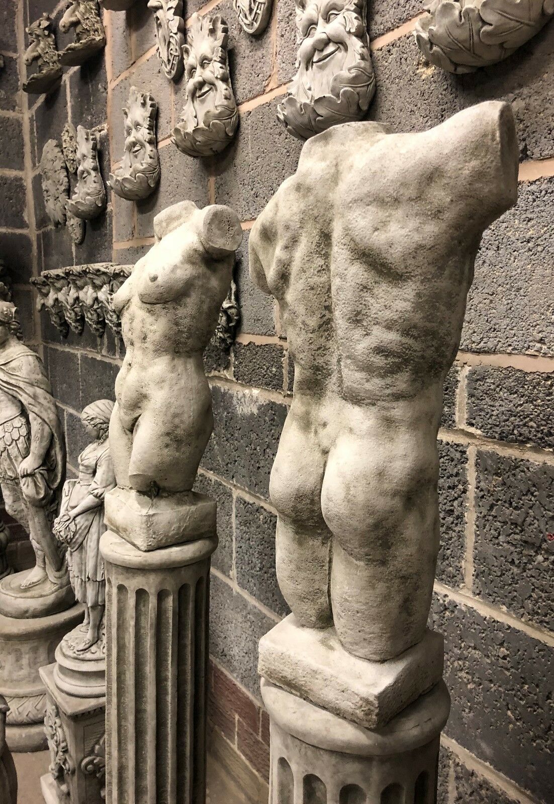 Rear angle of torso statues on stone columns, showcasing muscular and anatomical realism. Classic Grecian-inspired garden sculptures.