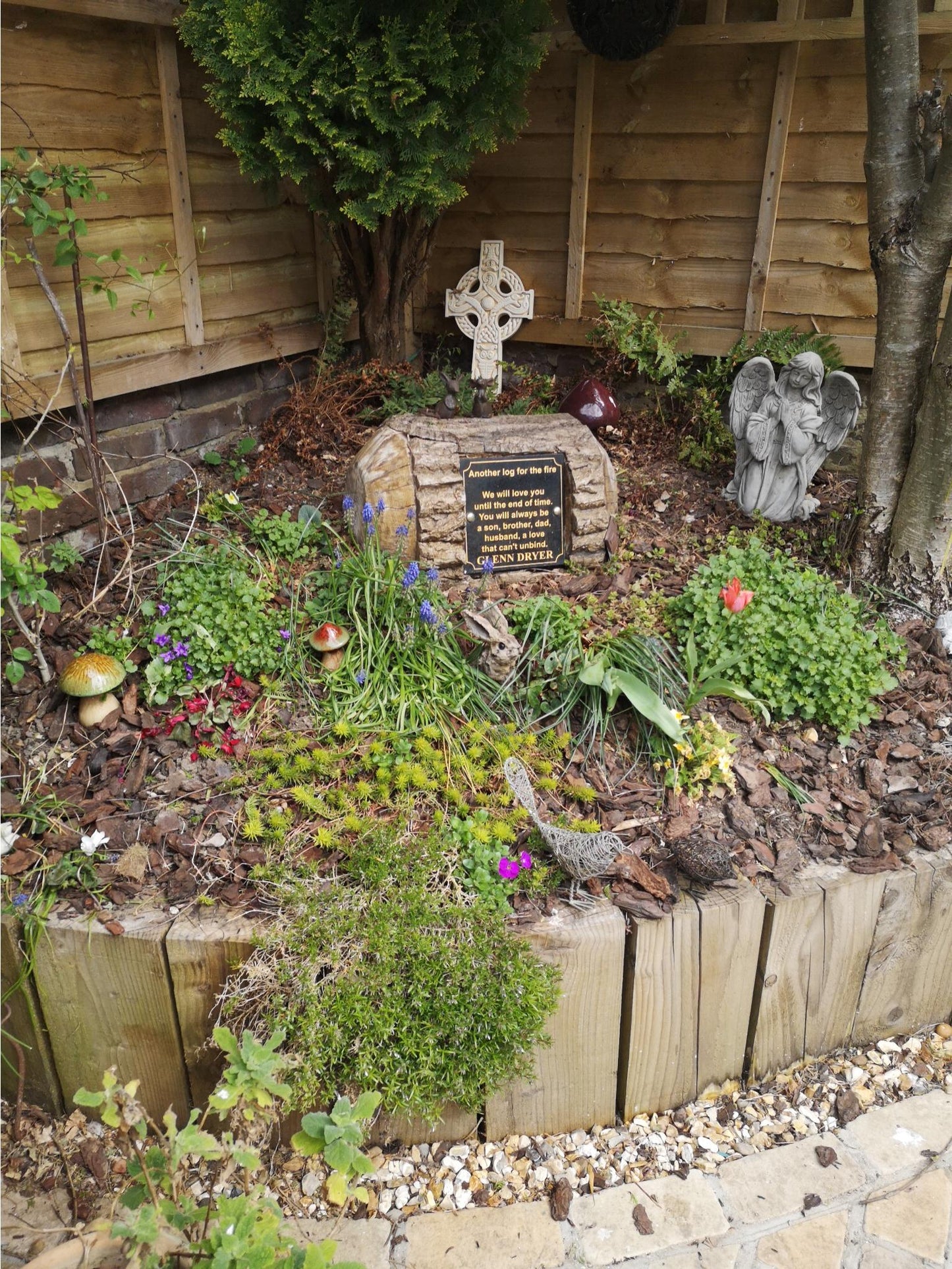 Stone Praying Angel Statue placed in a memorial garden with flowers and cross, enhancing spiritual and decorative ambiance.