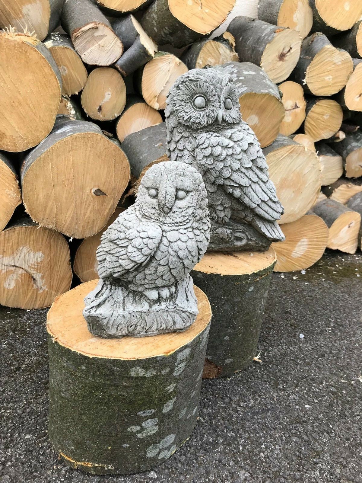 Pair of stone owl garden ornaments on wooden logs. Stone Owl Garden Ornaments - Mother & Baby crafted from durable limestone.