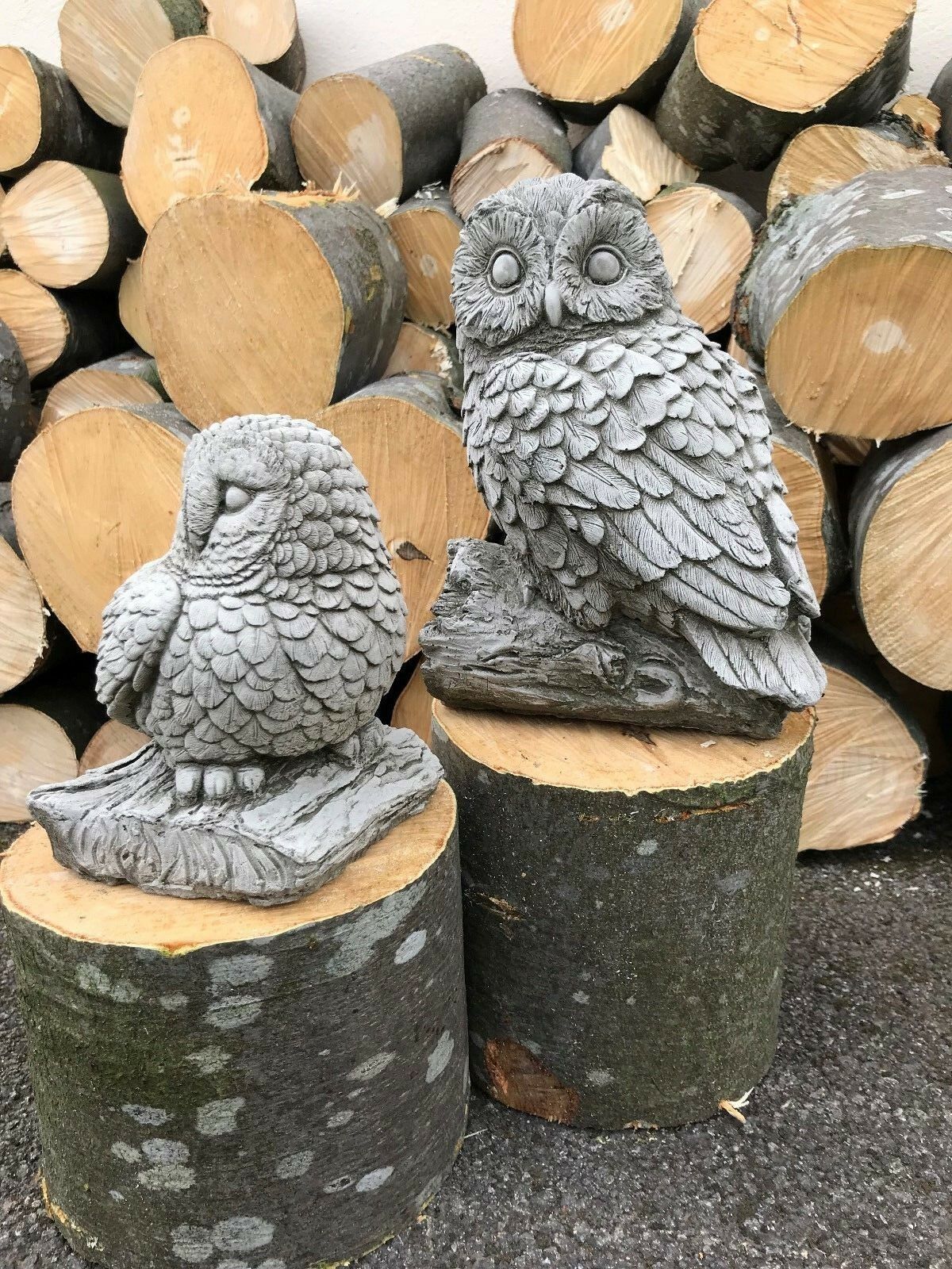 Detailed limestone owl pair on tree stumps. Stone Owl Garden Ornaments - Mother & Baby enhance rustic garden aesthetics.