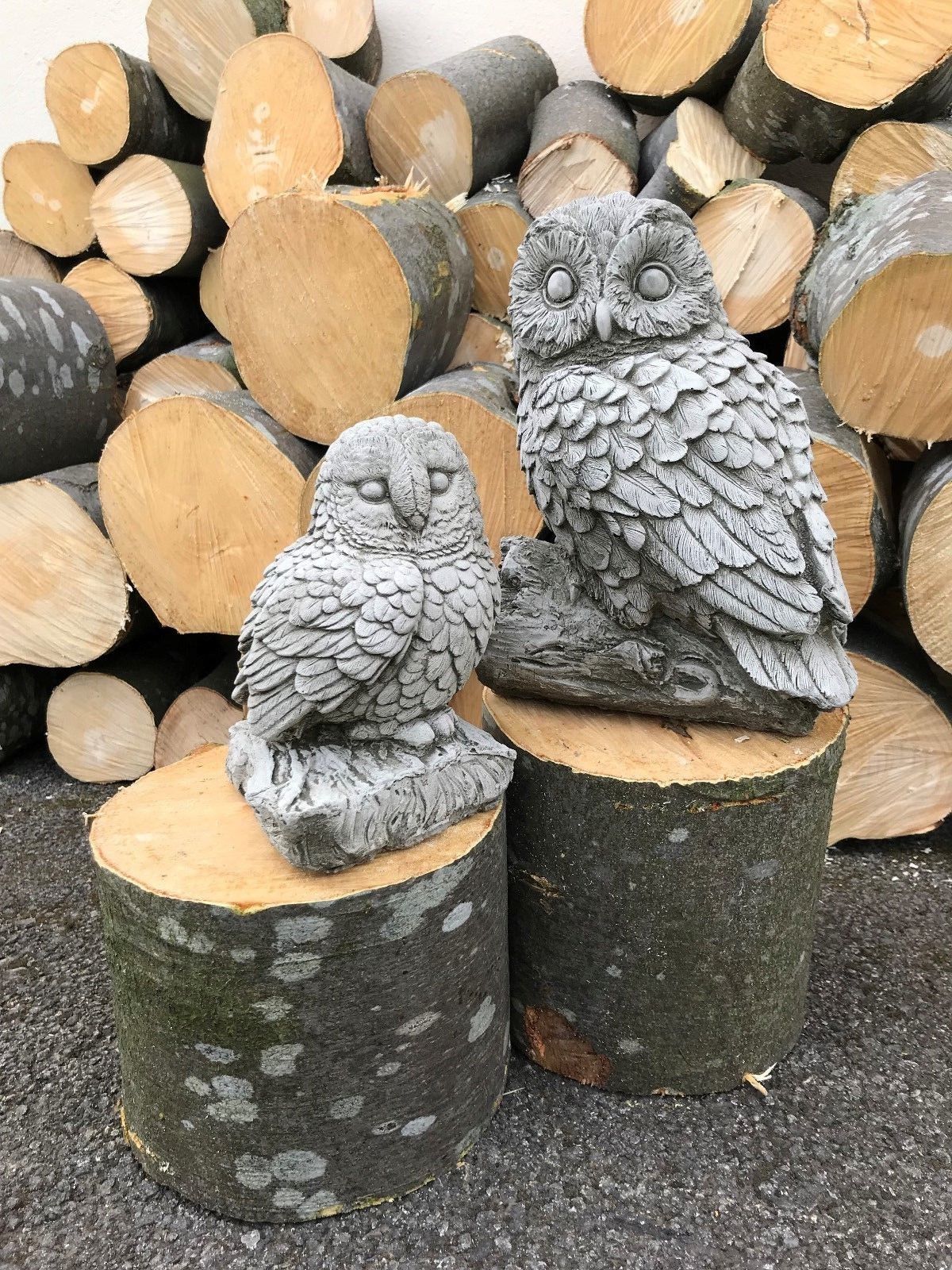 Mother and baby owl garden statues made from stone, set against stacked logs. Stone Owl Garden Ornaments - Mother & Baby collection.