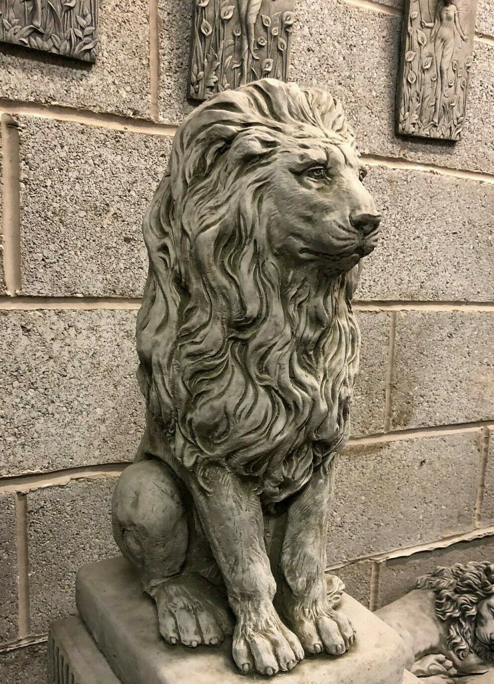 Side view of a stone lion statue with flowing mane and seated posture, crafted for durable outdoor garden decor.