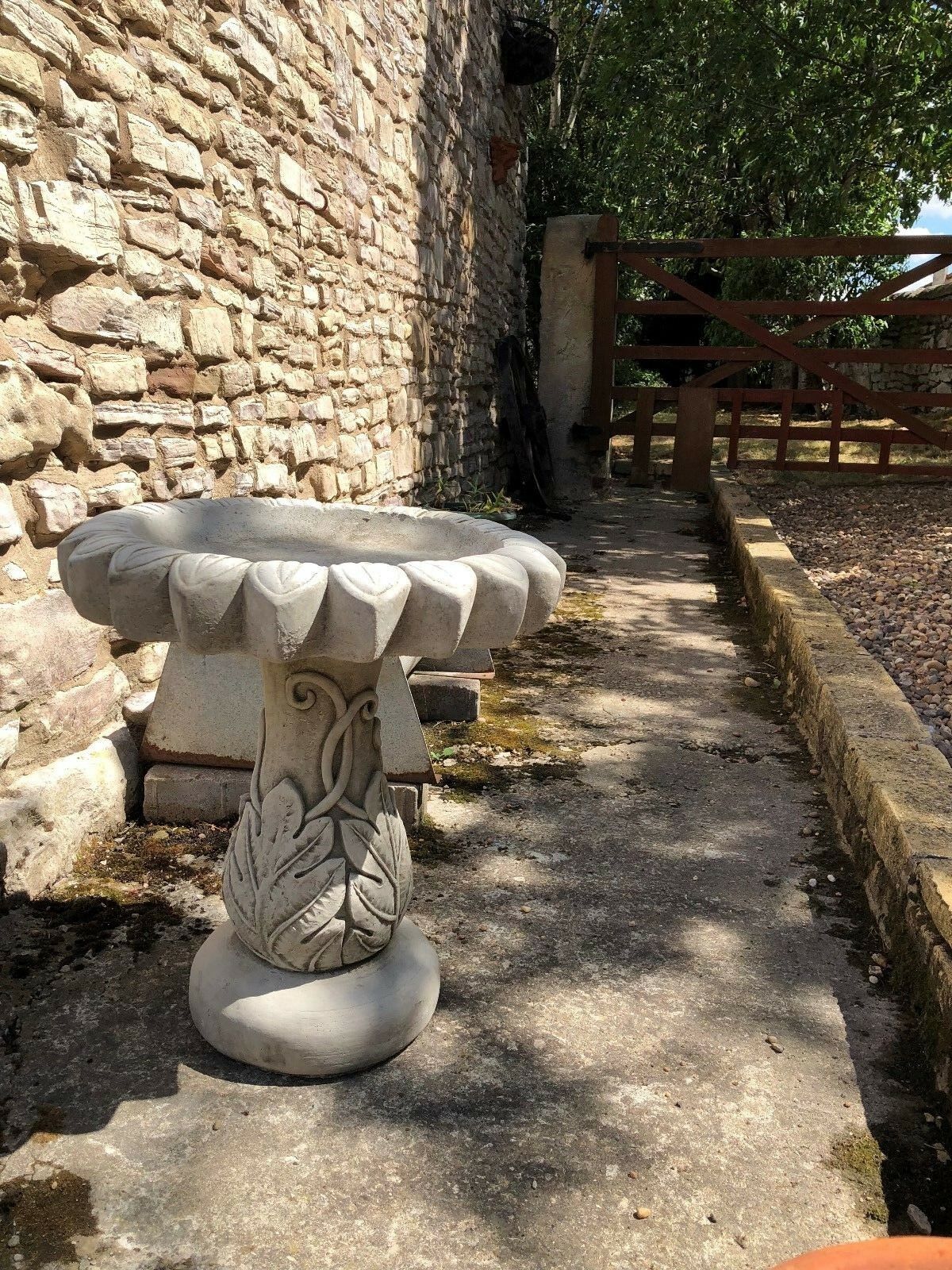 Stone sunflower bird bath sculpture with leaf base placed on a garden patio. Durable limestone design ideal for outdoor garden decor.