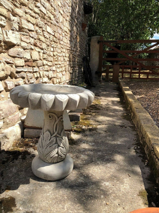 Stone sunflower bird bath sculpture with leaf base placed on a garden patio. Durable limestone design ideal for outdoor garden decor.