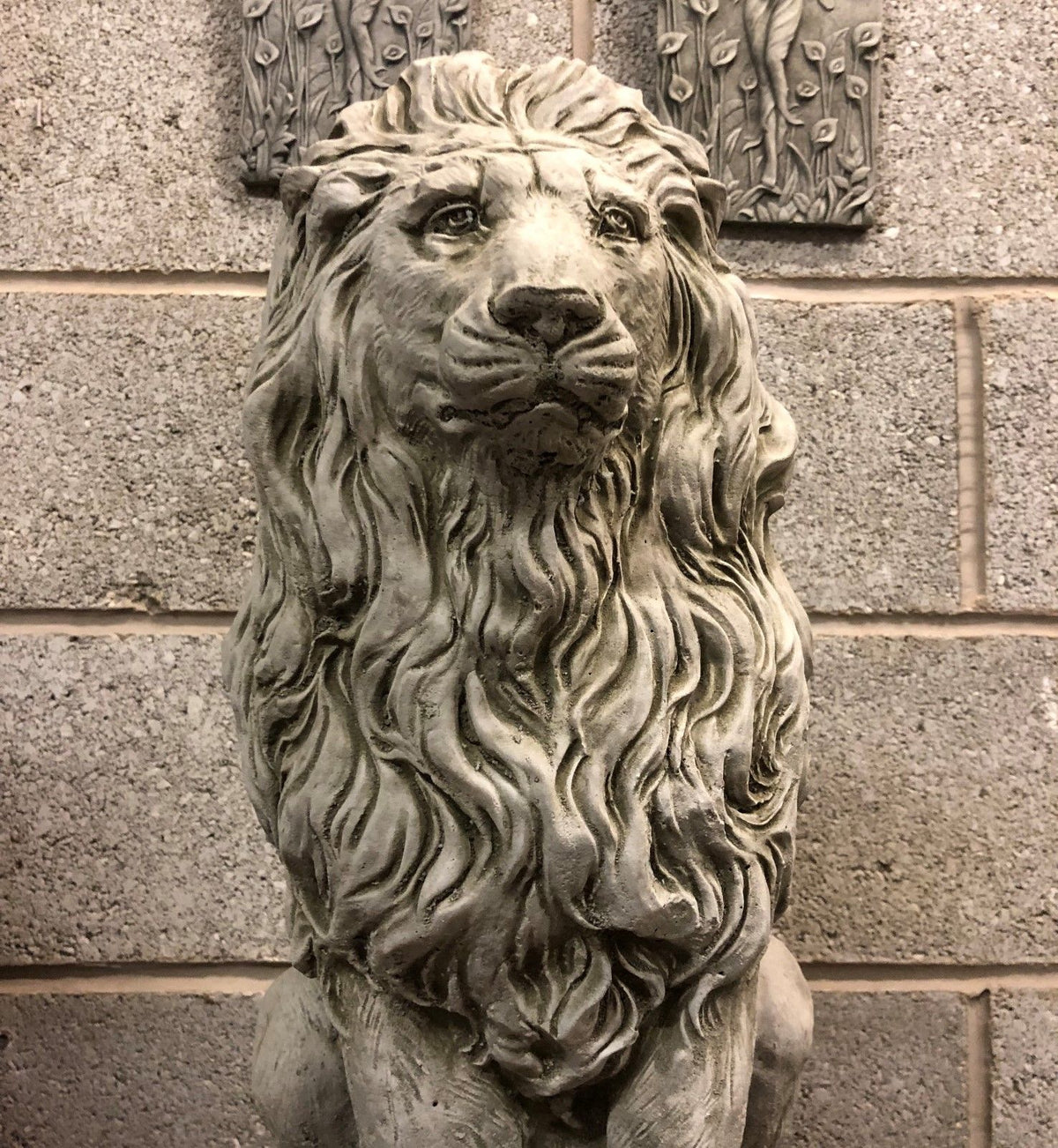 Close-up of lion statue head with detailed facial features and textured mane, part of a stone garden sculpture set.