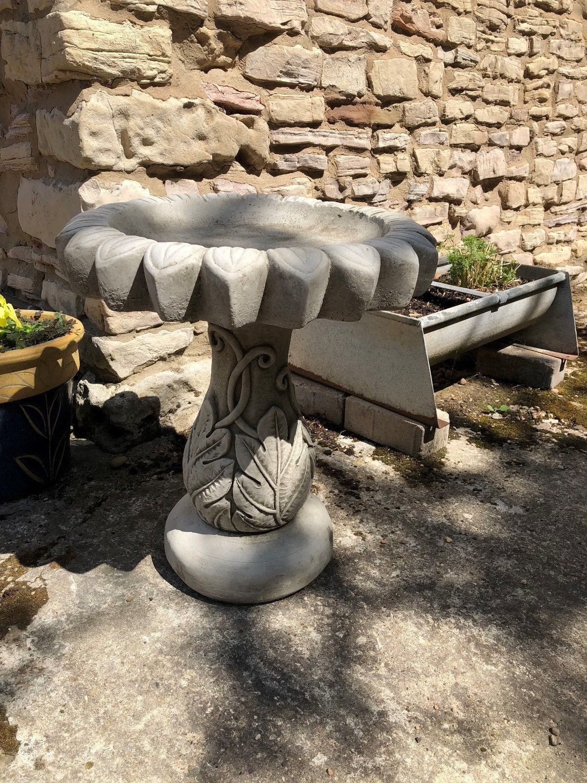 Close-up of stone sunflower bird bath featuring detailed leaf carvings on the pedestal. Weather-resistant garden sculpture for bird lovers.