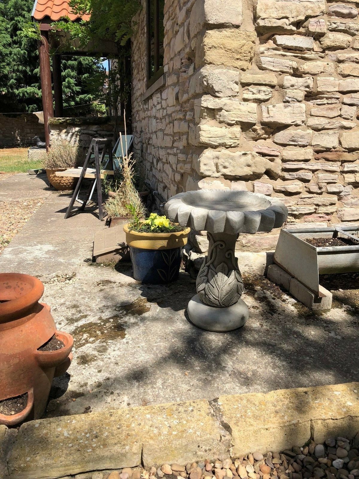 Sunflower-shaped stone bird bath in a rustic garden setting. Handmade limestone piece adds charm and function to outdoor decor.