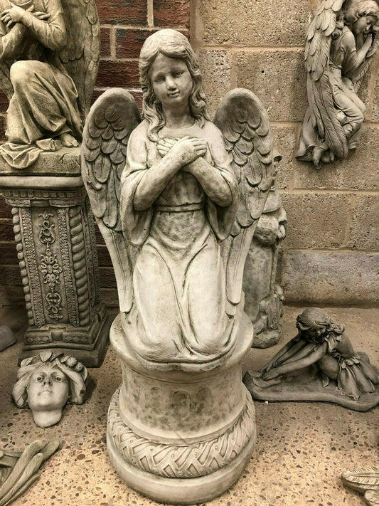Antique limestone angel statue kneeling on a pedestal with folded hands, ideal for garden decor or memorial settings in home and garden spaces.