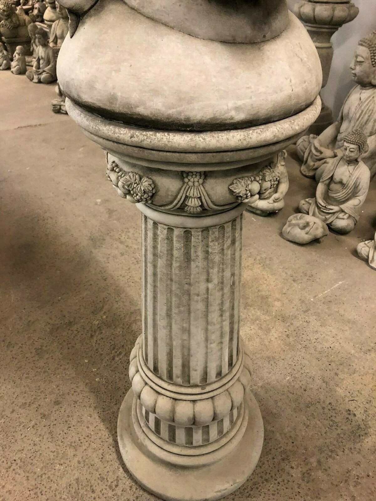 Close-up of the fluted stone pedestal base supporting Buddha Head Statue. Classical design enhances garden or home decor.
