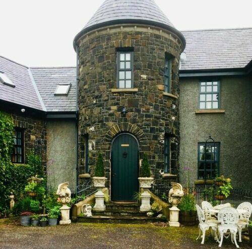 Full view of a stone house entrance with a pair of Bacchus urn planters on plinths, creating a grand garden feature.