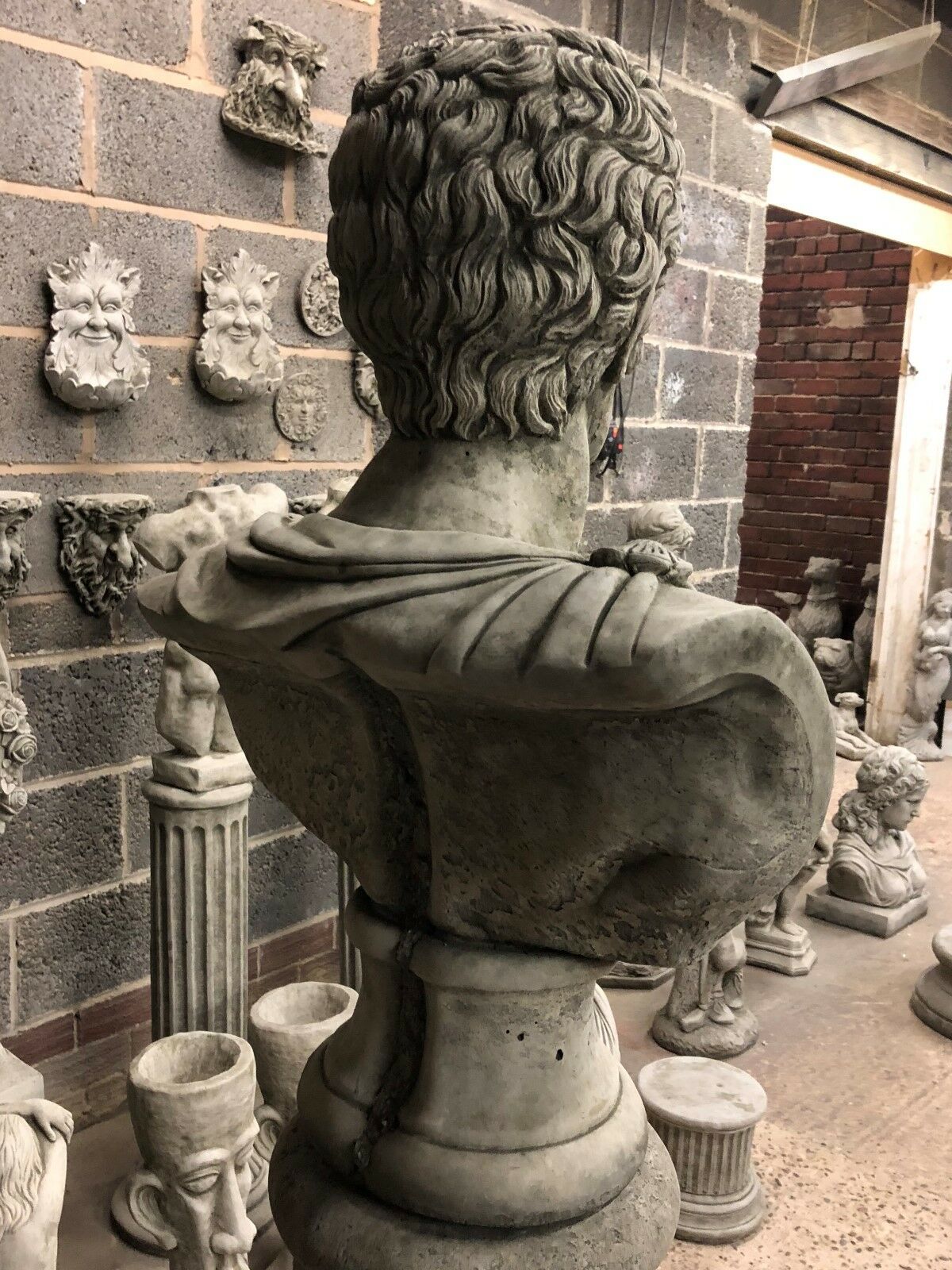 Rear view of Stone Marc Anthony Bust Statue showing sculpted hair and toga drape, mounted on a Roman-style limestone base for garden decor.