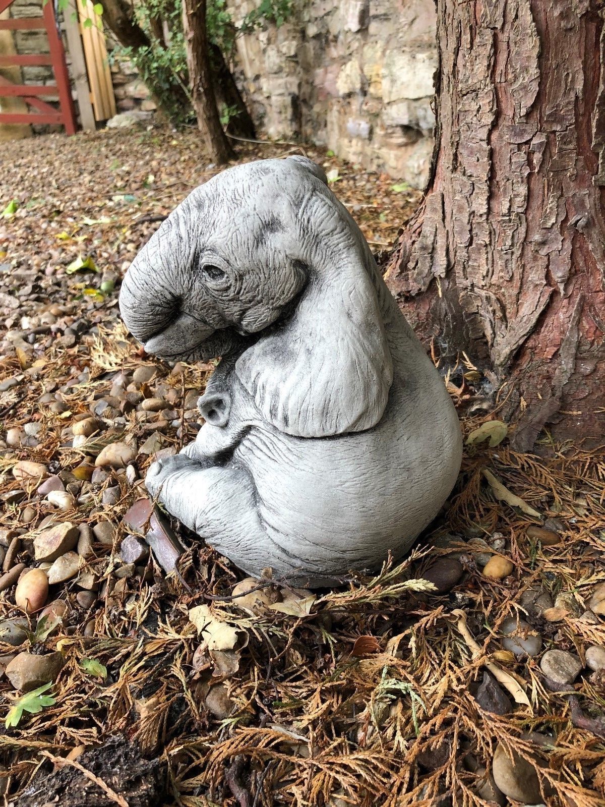 Side view of a stone baby elephant ornament nestled under a tree, perfect for garden lovers seeking unique animal-themed decor.