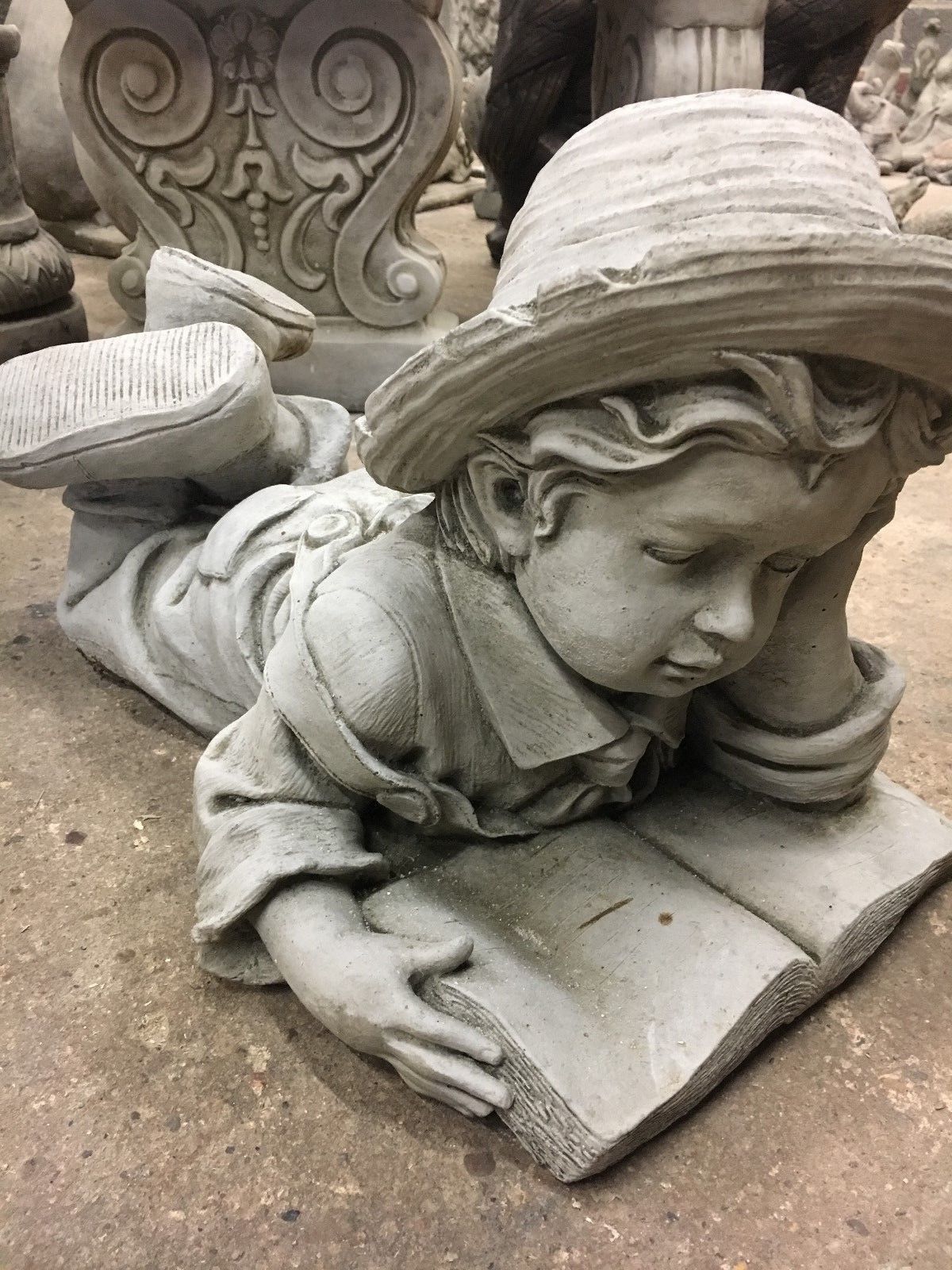 Detailed close-up of Reading Boy Statue with open book, handmade in stone for classic garden ornament appeal.